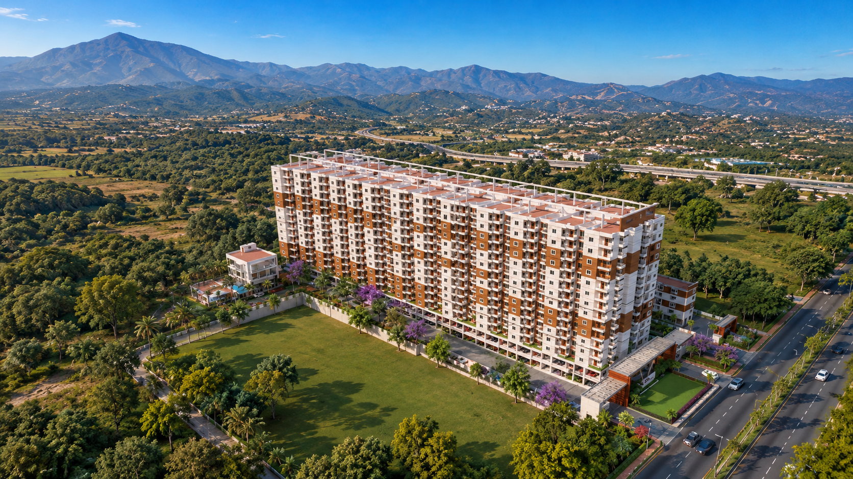 Coastal residential complex with pools, beachfront, roads, and distant mountains under clear blue sky.